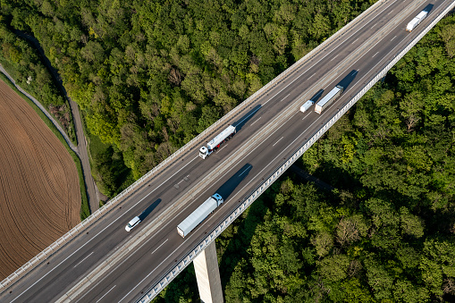 Aerial view of truck traffic on highway bridge over a valley covered with forest.