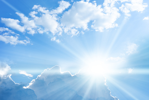 Blue sky background with clouds and sun rays coming out.