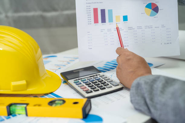 istock Asian engineer with architectural house plan project blueprint, graph and yellow helmet and engineering construction tools. 1470974026