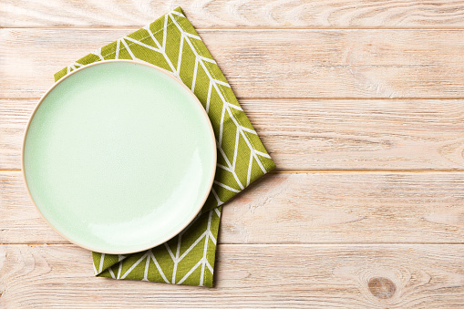 Top view on colored background empty round green plate on tablecloth for food. Empty dish on napkin with space for your design.