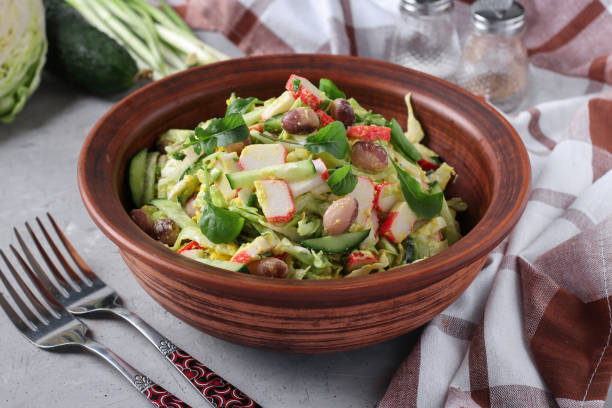 Salad with cabbage, crab sticks, beans, eggs and cucumber in brown bowl stock photo