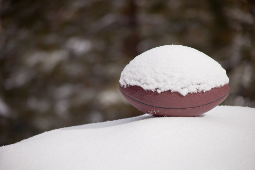 A close up of a football sitting on a snow hill with a green background.