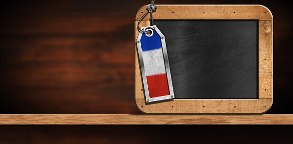 Empty blackboard with wooden frame and copy space, and a metal label with the French flag. On a wooden desk or shelf, front view.