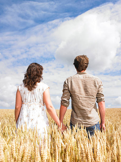 Rear view of a young man and woman standing in a wheat field and holding hands. Vertical format.