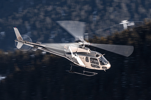 Grey AS350 helicopter flying in the French Alps near Courchevel Altiport