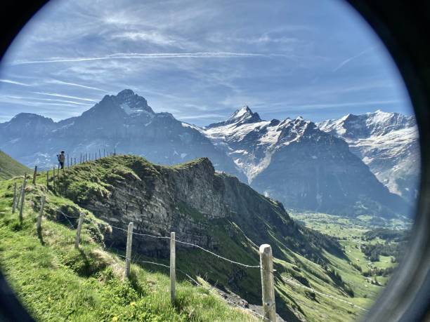 un escursionista si trova sopra una parete rocciosa a strapiombo che domina le alpi innevate dell'oberland bernese vicino a grindelwald, nella svizzera occidentale. - bernese oberland foto e immagini stock