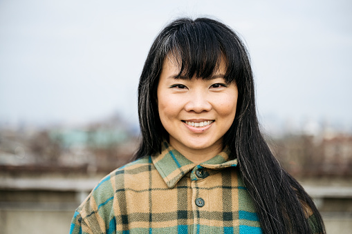 Head and shoulders view of woman with long black hair and bangs wearing plaid flannel shirt jacket and smiling at camera.