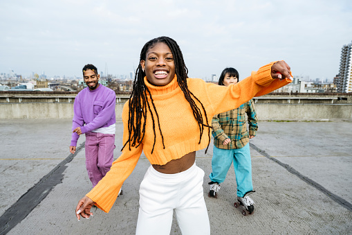 Candid portrait of jam skaters dancing on rooftop of concrete urban car park, smiling at camera, winter cityscape in background.