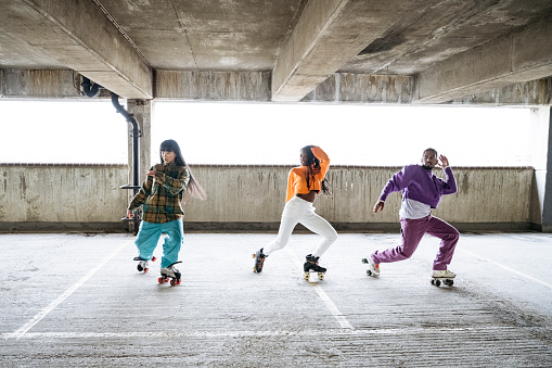 Full length front view of Black and Asian friends in 20s and 30s side by side and showing their moves in concrete garage.