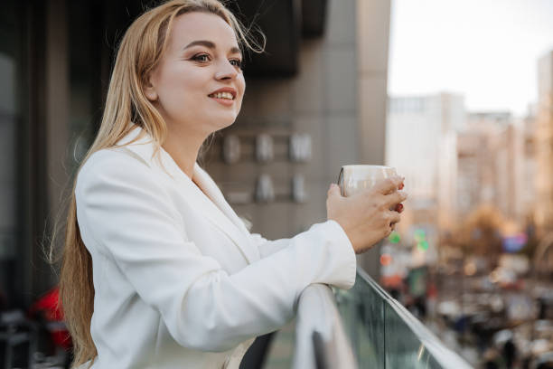istock Blond stylish woman at oversized white jacket drinking aroma coffee and relax on the modern city background 1470990137