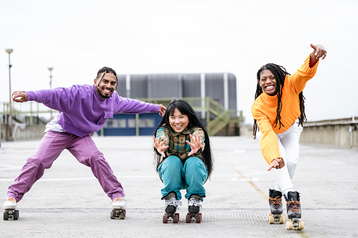 Action portrait of Asian and Black friends in 20s and 30s, wearing quad skates and casual winter clothing, smiling at camera.