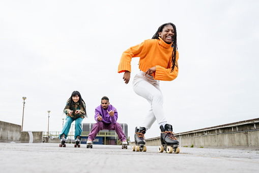 Full length view of laughing young Black woman followed by smiling friends as they exercise on rooftop of urban car park.