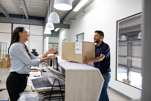 Happy Latin American business woman receiving a parcel at the office - delivery concepts