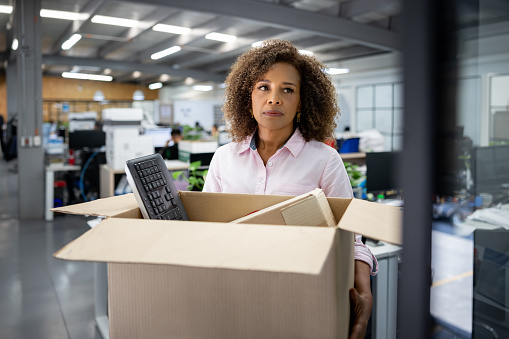 African American business woman being fired from her office and carrying a box with her belongings - unemployment concepts