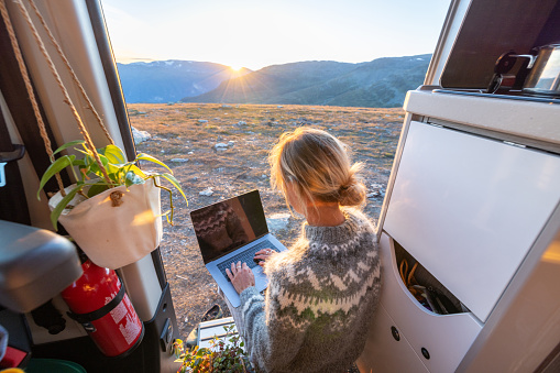 People travel, alternative homes concept. She carries her laptop, relaxing by the side door. Sunset time on top of mountain pass