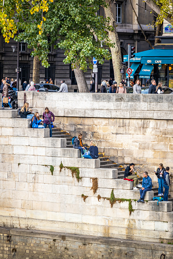 People sitting on the steps of a quay by the Seine river in Paris, France