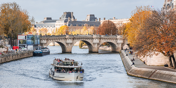 Vedettes de Paris tour boat cruising on the Seine river with lots of tourists onboard and the Pont Neuf bridge in the background in France