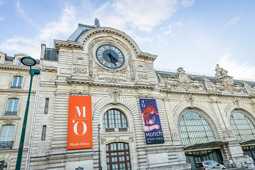 Munch exhibition poster and facade of the Orsay museum with view on the giant clock in Paris, France