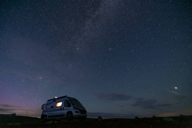 istock A camper van illuminated from inside standing on a high plateau, starry night without moon at night. 1471003913