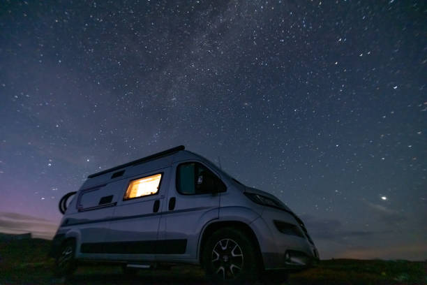 istock A camper van illuminated from inside standing on a high plateau, starry night without moon at night. 1471004754