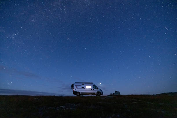 istock A camper van illuminated from inside standing on a high plateau, starry night without moon at night. 1471004756