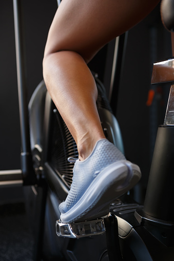 Female with pumped leg muscles riding on cross trainer machine in fitness club