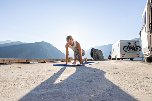 She practices on a yoga mat , view of camper van nearby. People travel having healthy routine concept.