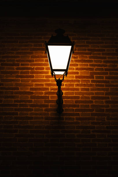 istock Vertical shot of a brick wall with a warm light lamp outdoors at night. 1471011843