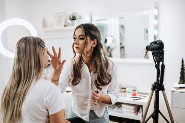 Makeup vlogger streaming at her studio Happy young woman streaming a beauty makeup vlog from home or workshop. Beautiful online content creator cosmetician applying makeup and explaining some work tools. Vlogging and online channel work. makeup artist stock pictures, royalty-free photos & images