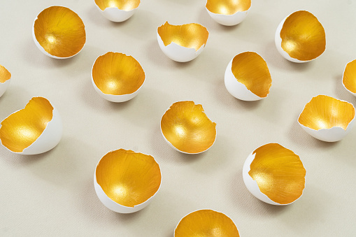 Golden eggshell on an ecru background. The concept of the modern vision of Easter. Happy Easter advertising banner. Abstract still life from eggshell.