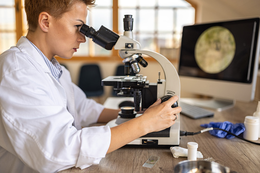 Female research scientist looking through a microscope while sitting in a medical laboratory office.