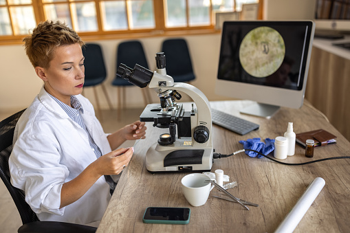 Female research scientist sitting in a medical laboratory office in front of microscope.