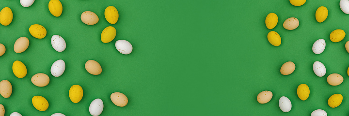 Happy Easter concept. Banner made from Easter candies, chocolate multi colored yellow and white eggs on green background. Flat Lay, top view, Copy Space