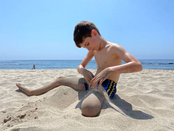 Caucasian boy digging a hole with a shovel in the sand at the beach