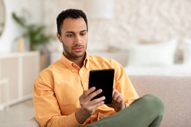 skupiony młody arab korzystający z tabletu cyfrowego w domu - middle eastern ethnicity men business digital tablet zdjęcia i obrazy z banku zdjęć