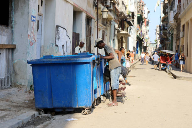 Havana, Cuba - March 2023: Beggar rummages in a trash can on a city street