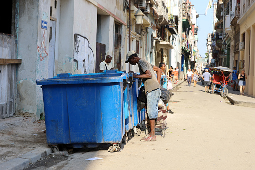 Havana, Cuba - March 2023: Beggar rummages in a trash can on a city street