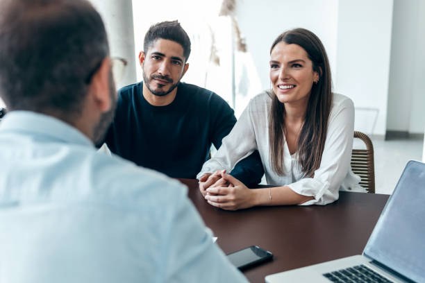 istock Handsome real-estate agent showing house plans on electronic tablet while talking to the couple about buying the house in the office. 1471035311