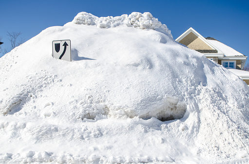 Luxury house hidden behind snowbank during day of winter. Road sign is buried under snow.