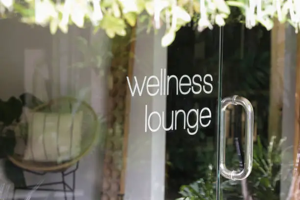 Wellness lounge beauty salon sign on the glass door with greenery reflexion