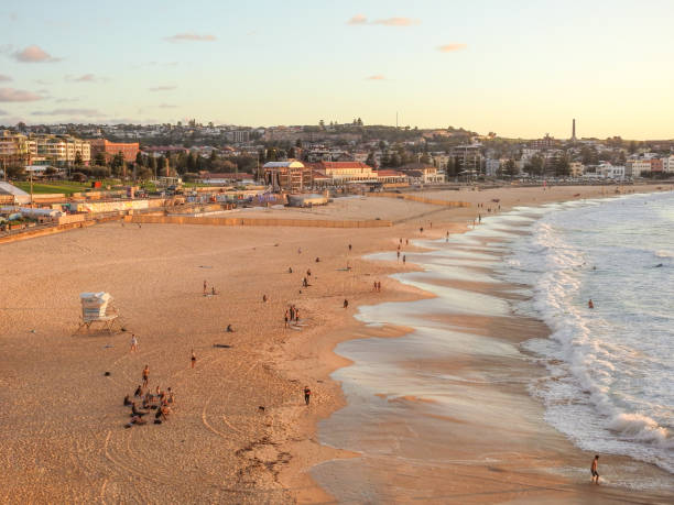 Bondi Beach Sunrise Autumn sunrise over Bondi Beach, Sydney. Later in the day, a dance party, named Bondi Beach Party, will be held on the beach as part of Sydney WorldPride 2023. The stage and area fenced off is visible in the centre of the beach. A group of people meditating is visible in the bottom left corner. Murals are visible along the promenade. This image was taken at sunrise on 4 March 2023. bondi beach sunrise stock pictures, royalty-free photos & images
