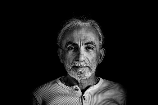 Man in his 60s.white hair,slightly beard.Looking at camera.Black background.Bust-up portrait.