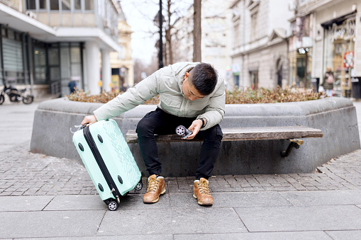 Man with broken suitcase sitting on the bench