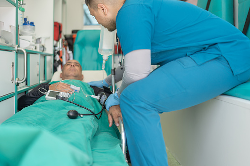 Doctor talking to a sick patient lying on a stretcher inside an ambulance on the way to the hospital