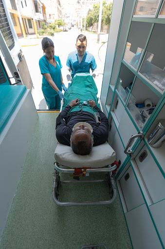 Interior of an ambulance with a patient on a stretcher and two doctors taking it off from outside in the door