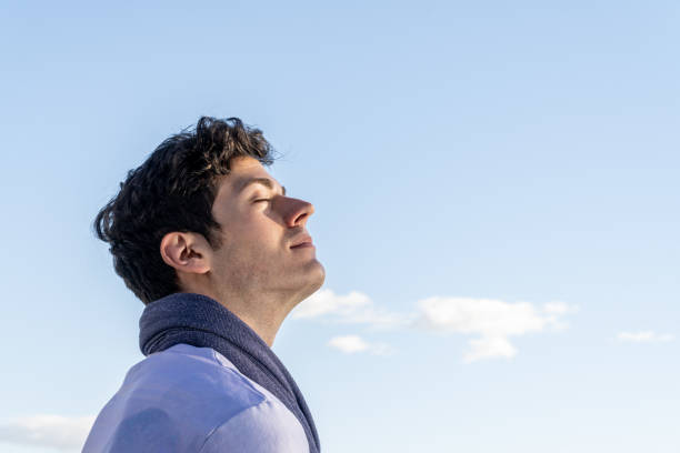 menino jovem de cabelos encaracolados isolado no fundo do céu claro e com os olhos fechados cheirando o céu azul - adult caucasian curly hair human face - fotografias e filmes do acervo