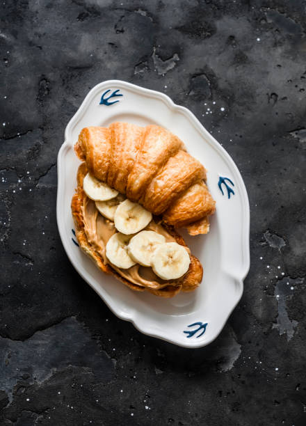 Croissant sandwich with peanut butter, banana on a dark background, top view