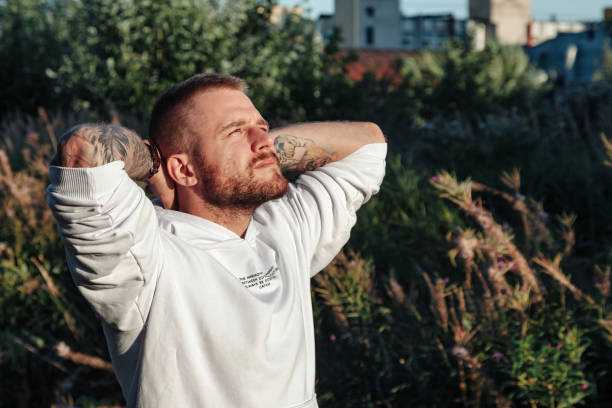 Relaxed bearded jewish man with tattoos in white jacket on nature, looking up. Male guy spending summertime in countryside outdoors. Lifestyle concept walk in fresh air in forest. Copy ad text space hombre judío barbudo relajado con tatuajes en chaqueta blanca en la naturaleza, mirando hacia arriba. chico masculino que pasa el verano en el campo al aire libre. concepto de estilo de vida caminar al aire libre en el bosque. copiar el espacio de texto d