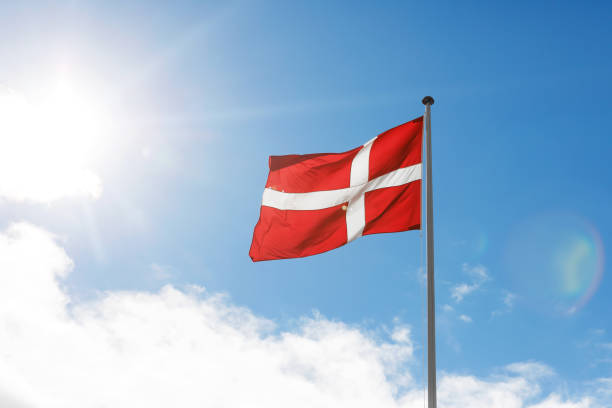 istock Danish flag waving on the blue sky sun glare background. 1471080658