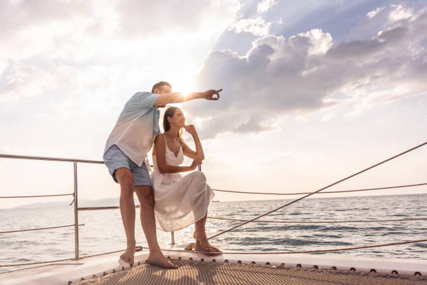 ヨットでパーティーをしながらシャンパンを飲む白人の若い夫婦。魅力的な男女がぶらぶらし、夏の日没時にカタマランボートを航行しながら記念日の新婚旅行を祝う。 - sunset yacht luxury sailboat ストックフォトと画像